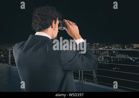 Kaufmann sieht sich die Stadt mit dem Fernglas während der Nacht. Zukunft und neue Business Opportunity Konzept Stockfoto
