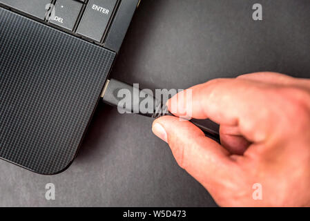 Männliche hand Sie ein USB Kabel zum Laptop closeup Draufsicht auf dunklem Hintergrund Stockfoto