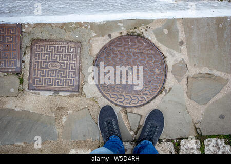 IOANNINA, Griechenland - 6 Juni, 2019 - männliche Füße in Blau staubigen sneakers Neben wenigen Schächte in Ioannina Insel auf dem See Pamvotida in der Nähe der beaut Stockfoto