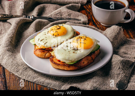 Toast mit Gemüse und Spiegeleier auf weißen Teller und Tasse Kaffee über Grau grobes Tuch. Stockfoto