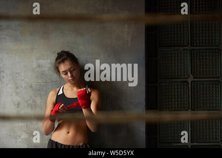Taille bis Portrait von harten Kämpferin Verpackung Hände im Stehen gegen die Betonwand in Boxing Club, kopieren Raum Stockfoto