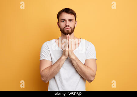 Hübscher junger Mann mit flehenden Bitten, Ausdruck, hält die Handflächen zusammen, bittet um Vergebung, Hilfe. Könnten Sie mir helfen, ich bitte Sie, mich zu heiraten. Vergib mir. Stockfoto