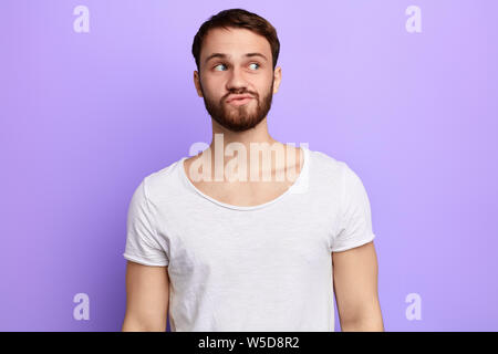 Junge lustig Bärtigen attraktive mman mit skeptischen Blicken, hat einige Zweifel, sieht beiseite, über blau Hintergrund isoliert. nach oben Porträt schließen. Platz für Text. Stockfoto