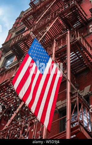 USA City, Blick auf eine Flagge der Vereinigten Staaten, die von einem Sandsteingebäude Feuerflucht in Little Italy, Downtown Manhattan, New York City hängt. Stockfoto