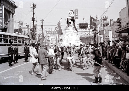 [1960s Japan - Bildnis des Nobusuke Kishi] - Japanische Männer in happi Mäntel tragen das Bildnis von Premierminister Nobusuke Kishi (岸信介, 1896 - 1987) Auf einem Tokio Straße bei einer Demonstration gegen den Vertrag über gegenseitige Kooperation und Sicherheit zwischen den Vereinigten Staaten und Japan (安保条約), 1960 (Showa 35). Stockfoto