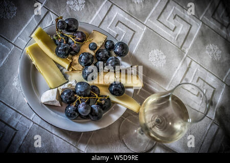 Ein Stillleben mit französischer Käse, Trauben und einem Glas Weißwein Stockfoto