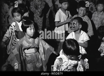 [1950er Jahre Japan - japanische Kinder Kinder an religiösen Festival] - Mädchen in der Yukata, und Jungen in westliche Kleidung, Tanz beim Bon-odori in Kobe, Hyogo Präfektur, 1959 (Showa 34). Die Buddhistischen Einhaltung der Obon (お盆) ehrt die Geister der Vorfahren. Stockfoto