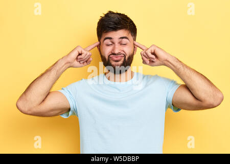 Lustiger Mann, die Gesichter, die Hände an die Schläfen. Nahaufnahme portrat, Guy Spaß. Isolierte gelben Hintergrund, Stockfoto