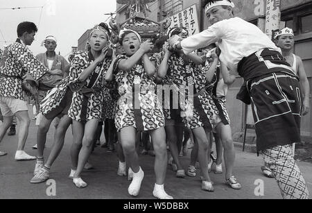 [1950er Jahre Japan - Japanische Jungen an einer Nachbarschaft Festival] - Jungen in der glücklichen Mäntel ein mikoshi Hebe, einem tragbaren Shinto Schrein, an einem Matsuri in Tengenji (天現寺), Tokyo 1958 (Showa 33). Stockfoto