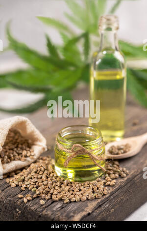 Hanf Öl in zwei Glas Glas und Flasche mit Getreide im Sack auf Holzbrett mit Blättern von Cannabis für den Hintergrund. Stockfoto