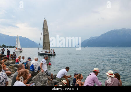 Vevey, Schweiz - 26. Juli 2019: Leute beobachten festliche Segelboote während der Fete des Vignerons 2019. Traditionelles Festival ist eine Hommage an die Traditionen des Weinsektors im Lavaux Wein Region. Organisiert einmal in 20-25 Jahren, einmal in einer Generation, seit dem 18. Jahrhundert. Es war, als die ersten lebendigen Tradition in der Schweiz erhielt UNESCO-Anerkennung geehrt. Festival findet vom 18.Juli bis 11. August 2019. Stockfoto