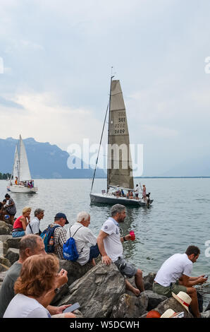 Vevey, Schweiz - 26. Juli 2019: Leute beobachten festliche Segelboote während der Fete des Vignerons 2019. Traditionelles Festival ist eine Hommage an die Traditionen des Weinsektors im Lavaux Wein Region. Organisiert einmal in 20-25 Jahren, einmal in einer Generation, seit dem 18. Jahrhundert. Es war, als die ersten lebendigen Tradition in der Schweiz erhielt UNESCO-Anerkennung geehrt. Festival findet vom 18.Juli bis 11. August 2019. Stockfoto