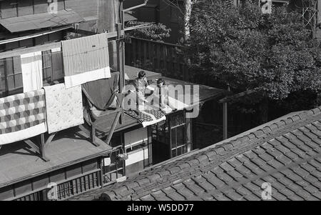 [1950er Jahre Japan - japanische Kinder auf einem Tokio Dach] - Kinder genießen die Sonne auf der Dachterrasse in Tengenji, Tokyo 1957 (Showa 32). Betten der Familie hängt auf einer Balustrade. Stockfoto