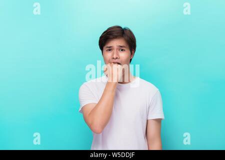 Wütend gereizte aggressive Jungen bärtigen Mann im weißen T-Shirt Beißen seiner Faust über blauer Hintergrund Stockfoto