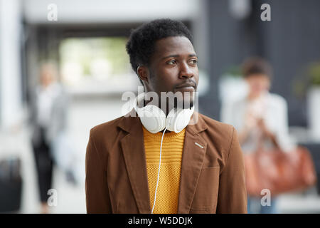 Nachdenklich inspiriert junge afro-amerikanischer Mann mit weissen Kopfhörer um den Hals laufen über Flughafen und rund um suchen Stockfoto