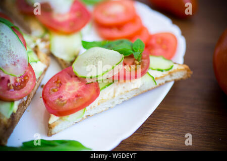 Leckeres Sandwich mit Quark einfügen, frischen Gurken und Tomaten auf rustikalen Holztisch Stockfoto