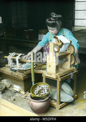 [1900s Japan - Japanische Frau Spinnen Seide] - eine junge japanische Frau dreht sich Seide zu Hause 20. Jahrhundert vintage Glas schieben. Stockfoto