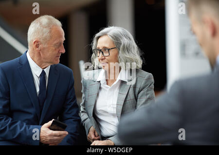 Ernst senior Geschäftsmann im Anzug in der Lobby sitzen und gestikulierend Hand besprechen Sie bei der Arbeit mit asiatischen Kollegen Stockfoto