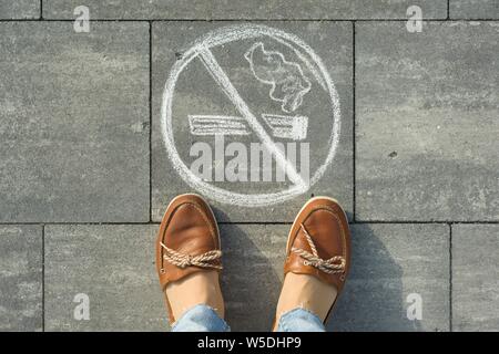 Weibliche Füße mit Bild nicht Rauchen auf den grauen Gehsteig gemalt. Stockfoto