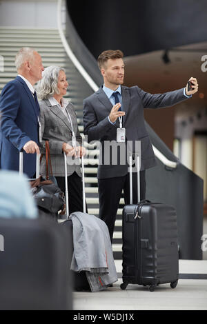 Hübscher junger Mann mit Abzeichen stehend mit Gepäck in der Lobby und dem Aufnehmen von Videos mit business forum Teilnehmer Stockfoto