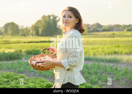 Outdoor Portrait von Bauer Frau mit Korb mit frischem huhn eier, Bauernhof, Gemüsegarten, Hintergrund, goldene Stunde Stockfoto