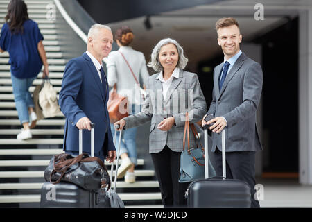 Gruppe positiver multi-ethnischen Business Menschen unterschiedlichen Alters stehend mit Gepäck im Flughafen und auf der Suche Stockfoto