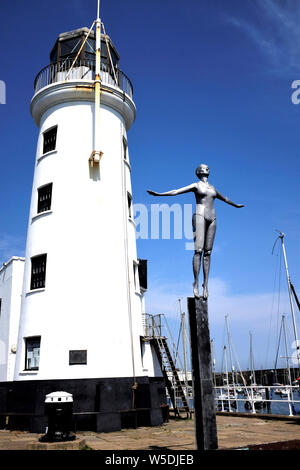 Scarborough, Yorkshire, UK. Juli 25, 2019. Verzinkter Stahl Statue einer Tauchen belle gegen den Leuchtturm am Ende der Vincent's Pier. Stockfoto