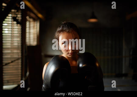 Dramatische Porträt der jungen Frau an der Kamera schaut mit Entschlossenheit beim Boxen Praxis im dunklen Zimmer, Kopie Raum Stockfoto