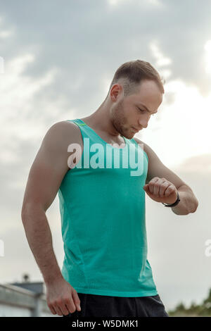 Portrait der kaukasischen Kerl in Azure t-shirt Fitness tracker Lesungen vor oder nach dem Joggen. Stockfoto