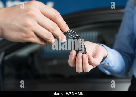 Verkäufer übergibt Autoschlüssel auf neue Besitzerin. Neue oder gebrauchte Fahrzeug Konzept zu kaufen. Stockfoto