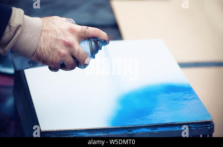 Hand gewagte artist Holding eine Flasche aerosol blaue Farbe und Drücken der Taste, zeichnet einen Jet auf einer weißen Leinwand Stockfoto