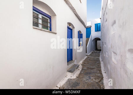 Schmale Straße zwischen Weiß traditionelle Häuser mit blauen Türen und Fenster im Stadtzentrum von Amorgos, Griechenland.