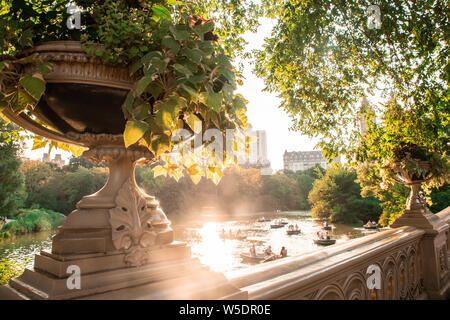 Sommer im Central Park in New York City von historischen Bogen Brücke mit unbekannten Menschen in Zeile Boote im See gesehen. Stockfoto