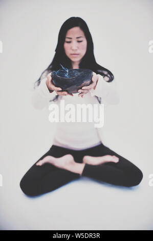 Schöne spirituelle asiatischen koreanisch-amerikanischen Frau sitzt im Lotussitz Holding eine Schüssel mit Wisch rauchen. Soft Focus Qualitäten. Stockfoto