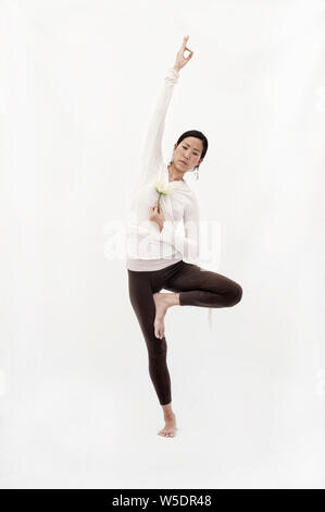 Schöne spirituelle asiatischen koreanisch-amerikanischen Frau mit einer Lotusblüte und Lastausgleich in einer Version von Yoga Baum darstellen. Stockfoto