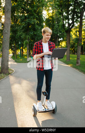 Junger Mann reiten auf Mini gyro Board mit Laptop Stockfoto