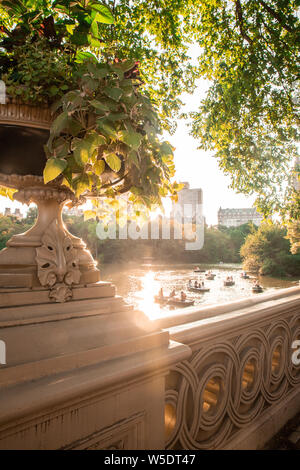 Sommer im Central Park in New York City von historischen Bogen Brücke mit unbekannten Menschen in Zeile Boote im See gesehen. Stockfoto