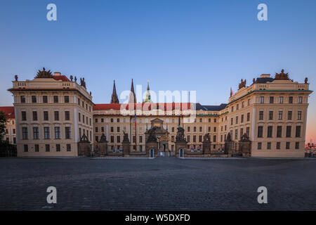 Eingang mit Vorplatz zur Prager Burg Hradschin Platz. Historisches Gebäude mit Zaun und Titans Skulpturen am Abend mit blauem Himmel Stockfoto