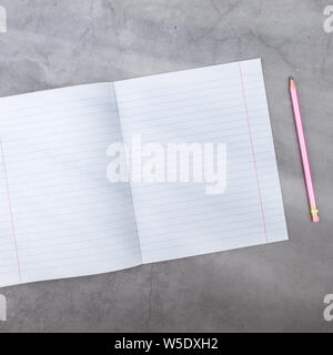 Flach, Ansicht von oben, Notebook, Bleistift auf einem grauen strukturierten Hintergrund. Strahlen von Licht von der Seite Stockfoto