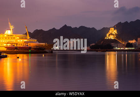 Am frühen Morgen Landschaft von einem Hafen in Muscat, eine voll beleuchteten Schiff mit ein Fort im Hintergrund mit Reflexion im Meerwasser geparkt. Stockfoto