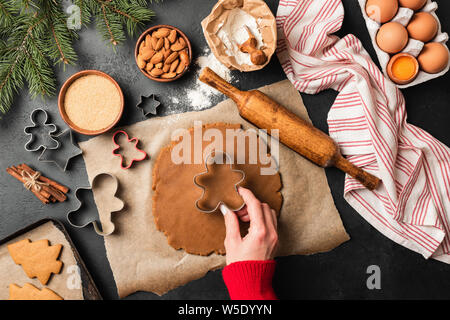 Weihnachten Lebkuchen Cookies Vorbereitung auf schwarzem Schiefer Tisch. Woman's Hand festliche Cookies mit Gewürzen Stockfoto