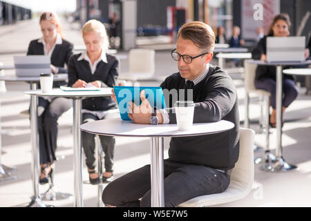 Viele Geschäft Leute im Café sitzen, auf Mann mit dem tablet pc konzentrieren Stockfoto