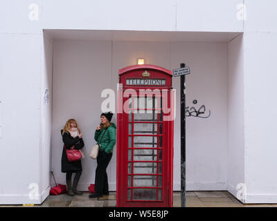 Zwei Menschen Schutz vor dem Regen neben einem klassischen Telefonzelle und kulturellen britische Ikone, in London. Stockfoto