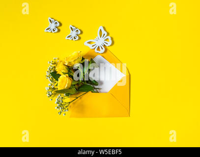 Gelbe Rosen und weißen Gypsophila in Umschlag und drei Holz- Schmetterlinge close-up auf gelben Hintergrund. Ansicht von oben, flach. Vorlage für eine Begrüßung Stockfoto