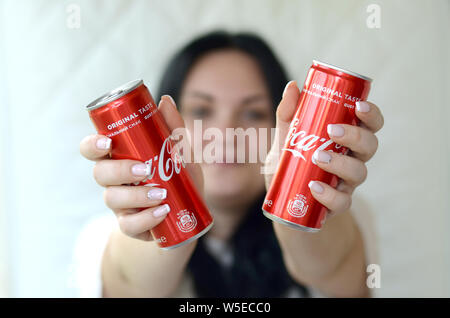Charkow, Ukraine - 15. JULI 2019: Glückliche Frau hält zwei alkoholfreie Coca-Cola Aluminium Blechdosen in der Garage. Coca Cola ist der Berühmteste Stockfoto