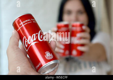 Charkow, Ukraine - Juli 15, 2019: Happy woman holding Paar Coca-Cola-Dosen in der garage Innen- und Außengewinde hand mit einem können im Vordergrund. Coca Cola ist Stockfoto