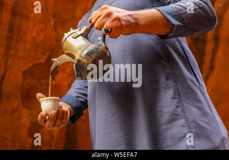 Beduinemann gießt Kaffee in eine Schale von einer traditionellen authentischen Kaffeekanne. Stockfoto