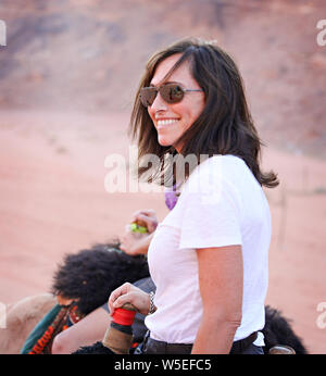 Eine Brünette weiß Frau reitet auf einem Kamel durch die Wüste des Wadi Rum, Jordanien. Stockfoto