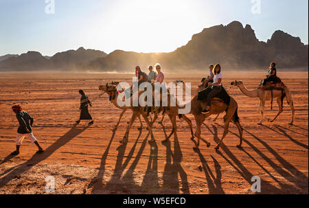 Eine Gruppe von Frauen reiten Kamele mit Beduinen durch die Wüste des Wadi Rum, Jordanien. Stockfoto