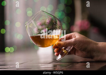 Weibliche hand Glas Cognac. Entspannung Konzept. Kurze von Weinbrand in elegantes Glas mit Platz für Text. Starke alkoholische Getränk. Stockfoto